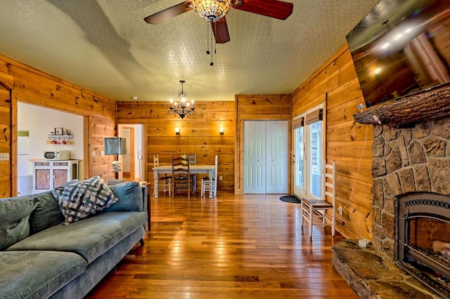 living area with wood-type flooring, wood walls, a textured ceiling, and ceiling fan with notable chandelier