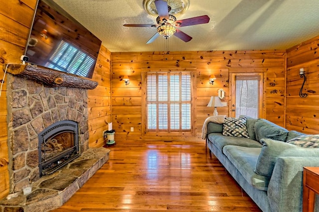 living area featuring wood-type flooring, a fireplace, a ceiling fan, and a textured ceiling