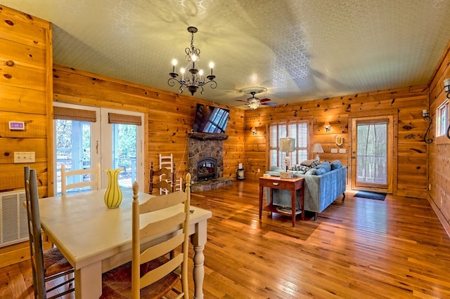 dining area featuring wood-type flooring, ceiling fan with notable chandelier, a textured ceiling, and a stone fireplace