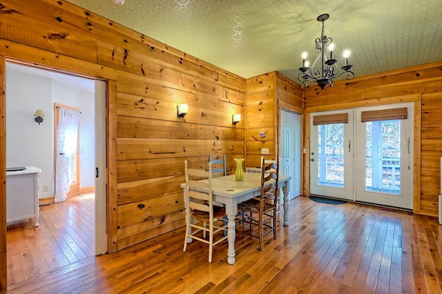 dining room with hardwood / wood-style flooring, wooden walls, a textured ceiling, and an inviting chandelier