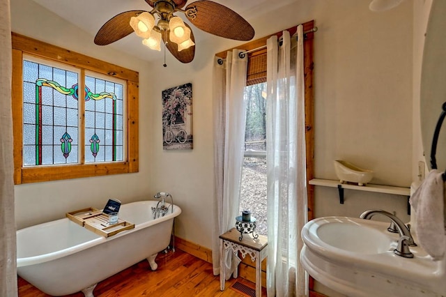 full bath with a sink, wood finished floors, a ceiling fan, a freestanding bath, and baseboards