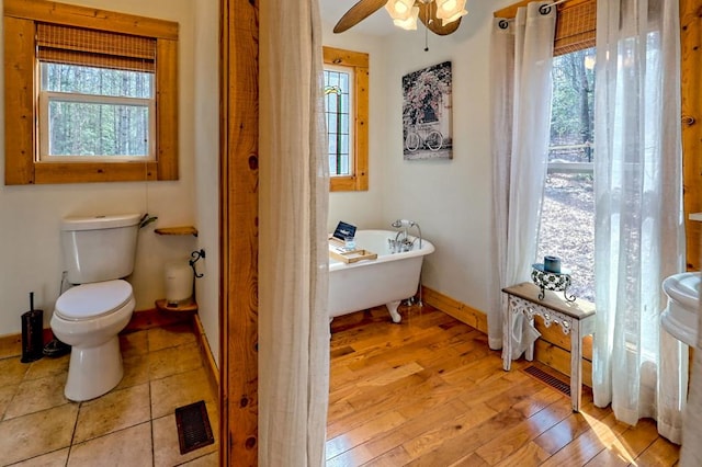 full bathroom with toilet, visible vents, baseboards, a soaking tub, and hardwood / wood-style floors