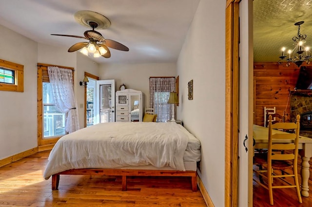 bedroom with baseboards, wood finished floors, access to exterior, a fireplace, and ceiling fan with notable chandelier