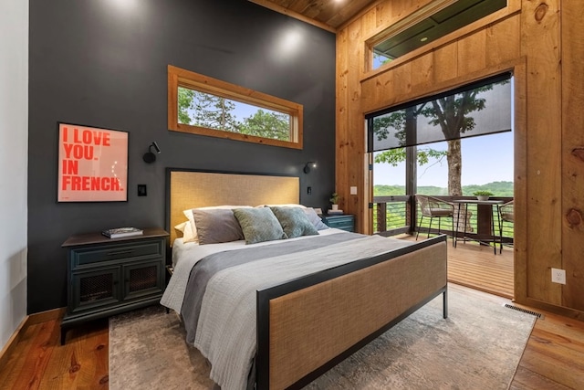 bedroom with hardwood / wood-style floors, access to exterior, a towering ceiling, and wooden ceiling