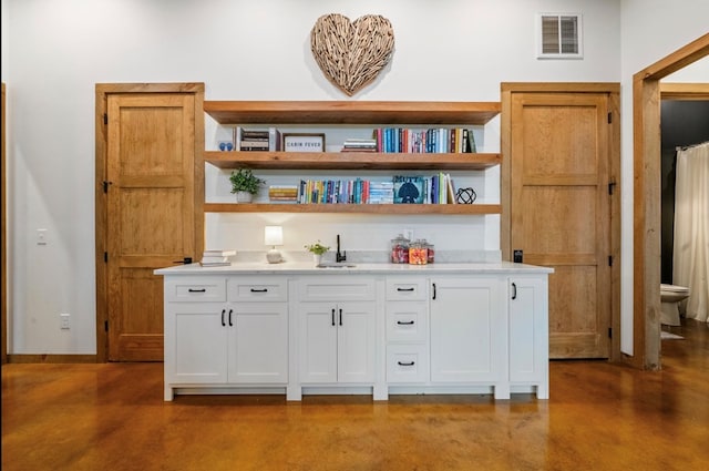 bar featuring white cabinets, concrete flooring, and sink