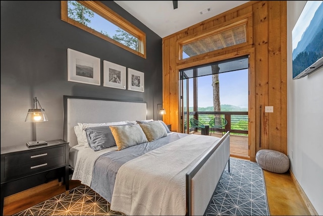 carpeted bedroom with access to exterior, a towering ceiling, wooden walls, and multiple windows