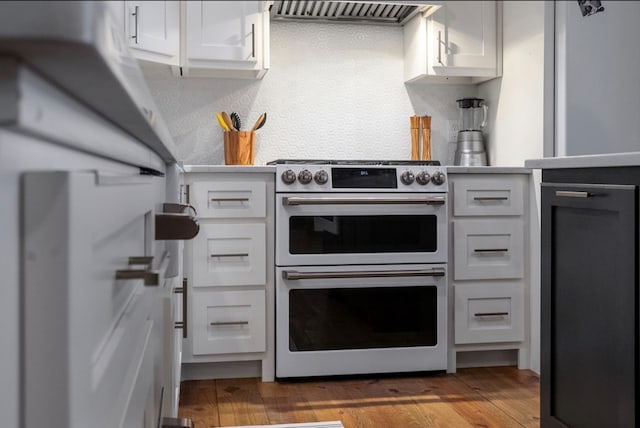 kitchen featuring dark wood-type flooring, exhaust hood, white refrigerator, range with two ovens, and white cabinetry