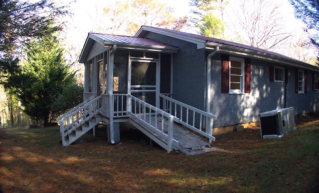 view of front of house featuring a front lawn, central air condition unit, a sunroom, and metal roof