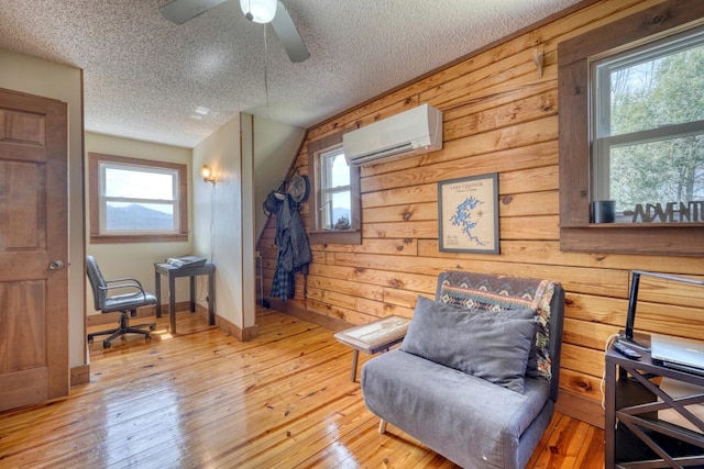 living area featuring an AC wall unit, ceiling fan, a healthy amount of sunlight, and light wood-type flooring