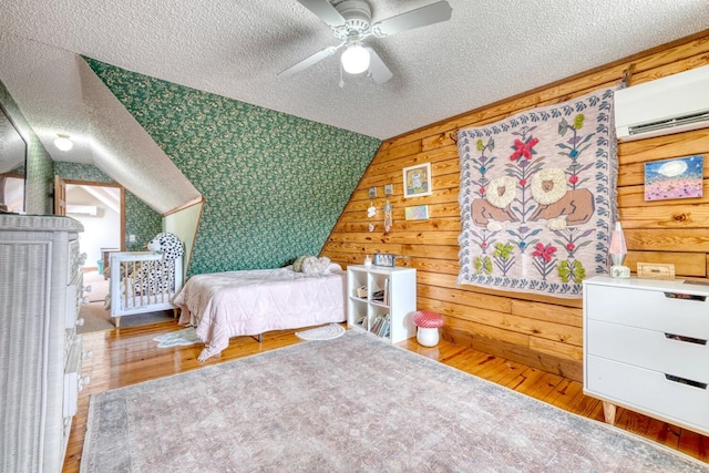 bedroom featuring a wall mounted air conditioner, lofted ceiling, hardwood / wood-style flooring, ceiling fan, and a textured ceiling