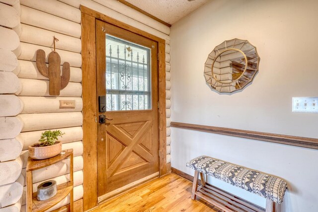 interior space featuring a textured ceiling, log walls, and light hardwood / wood-style flooring