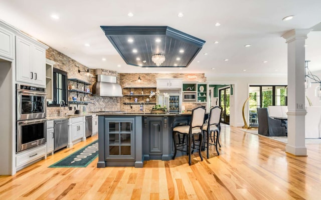 kitchen featuring a breakfast bar, stainless steel appliances, white cabinets, wall chimney range hood, and tasteful backsplash