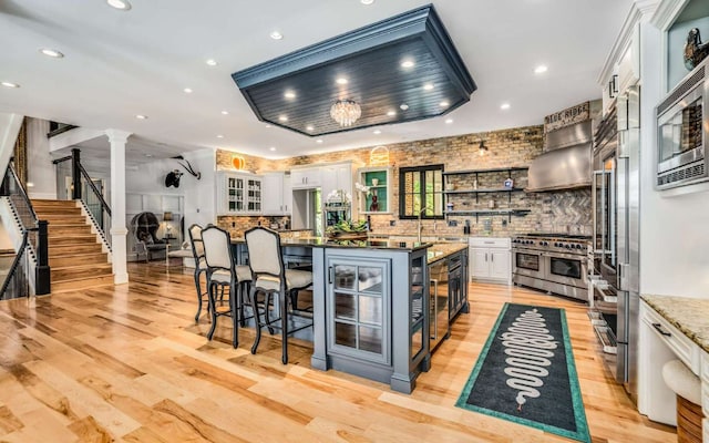 kitchen featuring ornate columns, a breakfast bar area, white cabinetry, a center island with sink, and stainless steel appliances