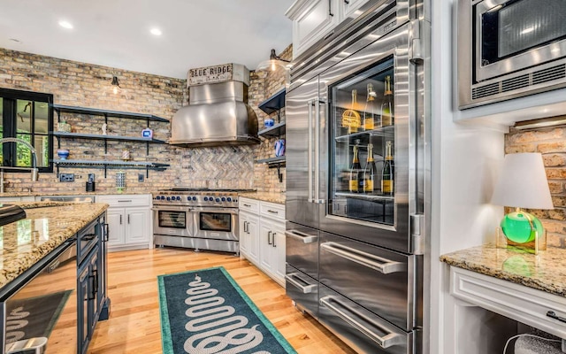 kitchen with light wood-type flooring, white cabinetry, wall chimney range hood, and built in appliances