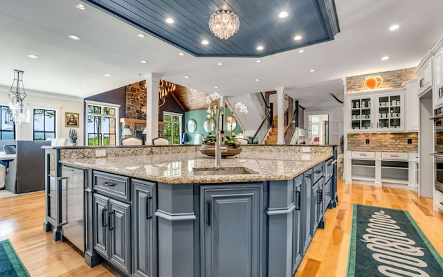 kitchen with an inviting chandelier, a kitchen island with sink, light wood-type flooring, and white cabinetry