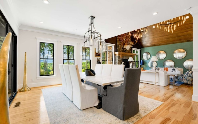 dining space with light hardwood / wood-style floors, wood ceiling, a stone fireplace, crown molding, and lofted ceiling