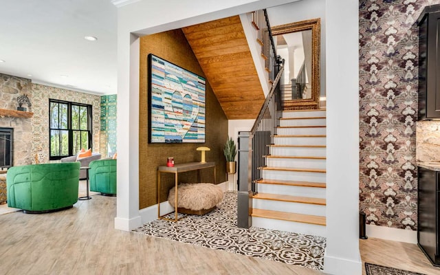 stairs featuring wood ceiling, a stone fireplace, and light hardwood / wood-style flooring