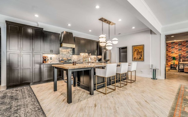 kitchen featuring hanging light fixtures, a breakfast bar, custom exhaust hood, light hardwood / wood-style flooring, and a center island with sink