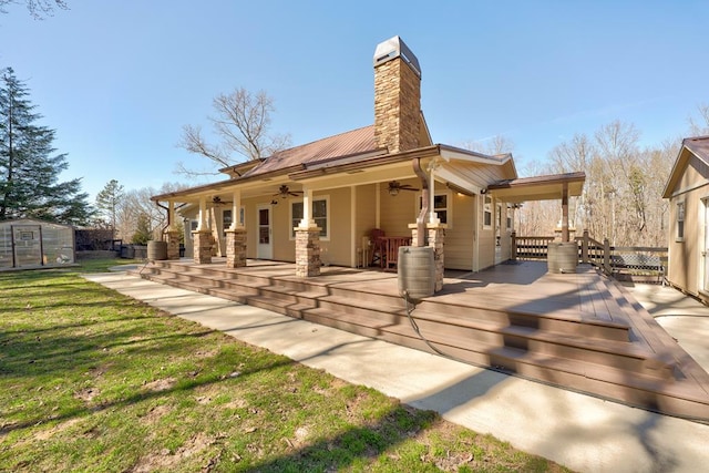 back of property with ceiling fan, a chimney, metal roof, a yard, and an outdoor structure