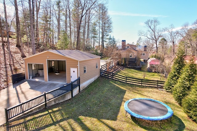 view of yard with an outbuilding, a garage, fence, a pole building, and a trampoline