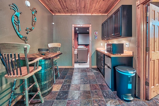 kitchen featuring a textured wall, wooden ceiling, butcher block countertops, baseboards, and stone tile flooring