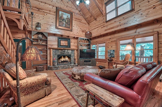 living area with high vaulted ceiling, a stone fireplace, wooden walls, wood finished floors, and wood ceiling