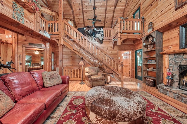 living area with wood ceiling, a stone fireplace, light wood-type flooring, wood walls, and high vaulted ceiling