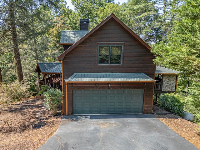 exterior space with an attached garage, metal roof, a chimney, and aphalt driveway