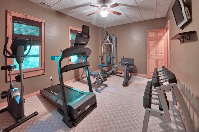 workout room with ceiling fan, a textured wall, a paneled ceiling, baseboards, and carpet