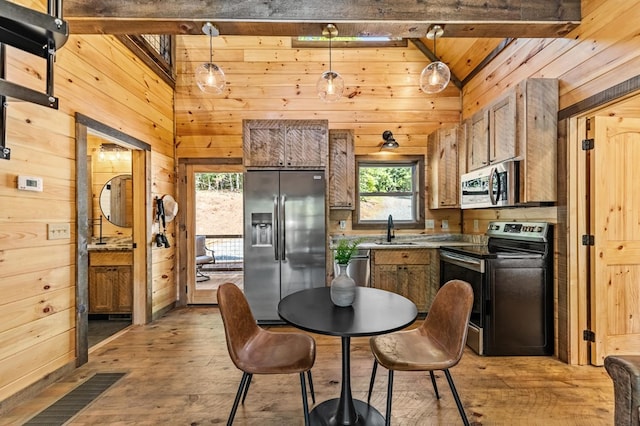 kitchen with appliances with stainless steel finishes, sink, hardwood / wood-style flooring, wooden walls, and vaulted ceiling with beams