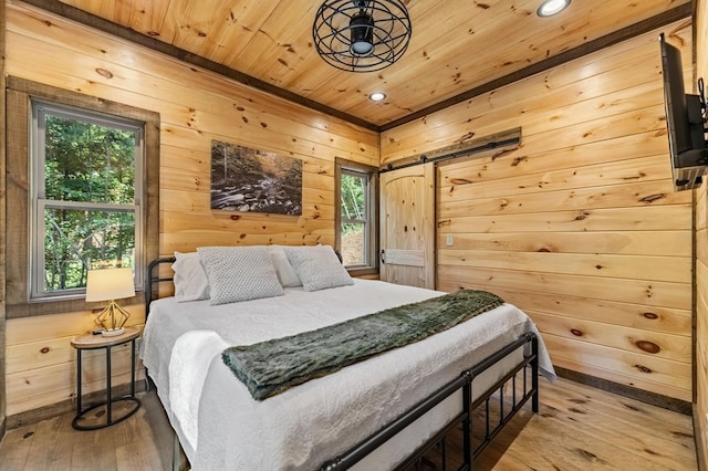 bedroom featuring a barn door, multiple windows, wooden ceiling, and light hardwood / wood-style flooring