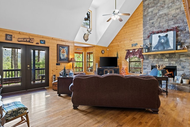 living room featuring hardwood / wood-style flooring, wooden walls, a stone fireplace, and french doors