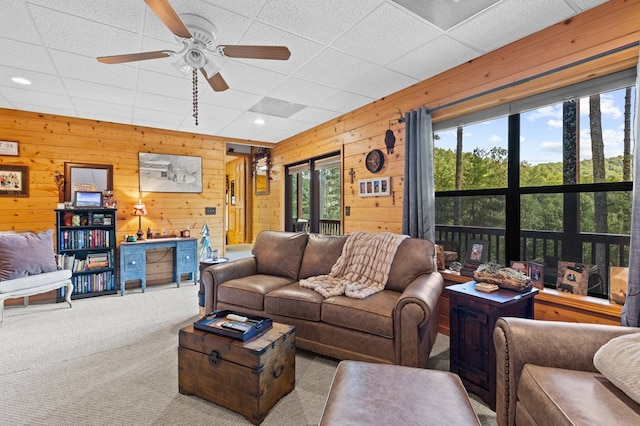 living room featuring light carpet, wooden walls, ceiling fan, and a paneled ceiling