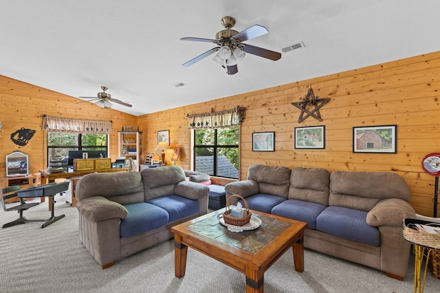 carpeted living room with ceiling fan, a healthy amount of sunlight, wooden walls, and vaulted ceiling