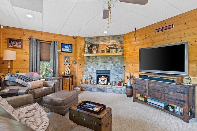 carpeted living room featuring a paneled ceiling, wooden walls, and a stone fireplace