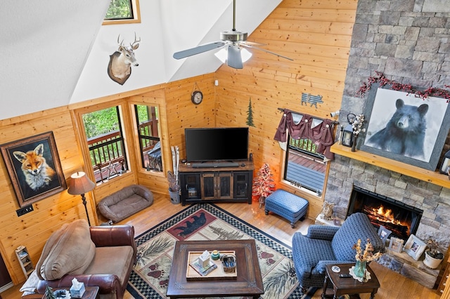 living room with a high ceiling, a stone fireplace, hardwood / wood-style flooring, and wooden walls