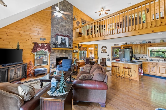 living room featuring ceiling fan, a stone fireplace, wooden walls, and light hardwood / wood-style floors