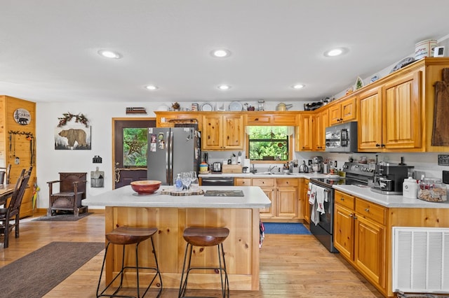 kitchen with sink, a breakfast bar area, black appliances, light hardwood / wood-style floors, and a kitchen island