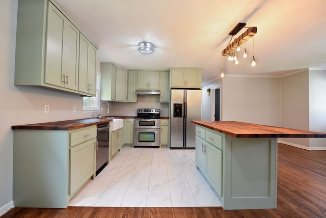 kitchen featuring decorative light fixtures, butcher block counters, sink, green cabinetry, and stainless steel appliances