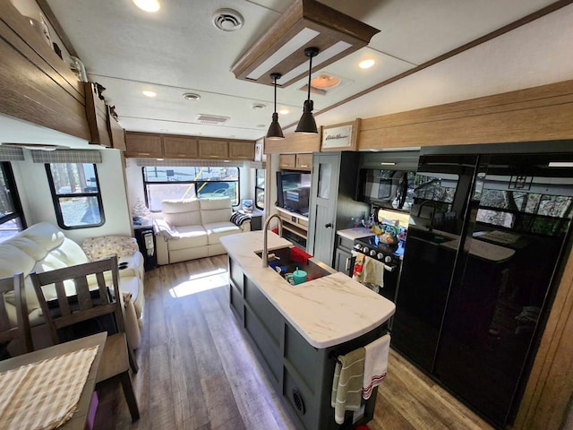 kitchen with pendant lighting, dark wood-style flooring, visible vents, an island with sink, and black appliances