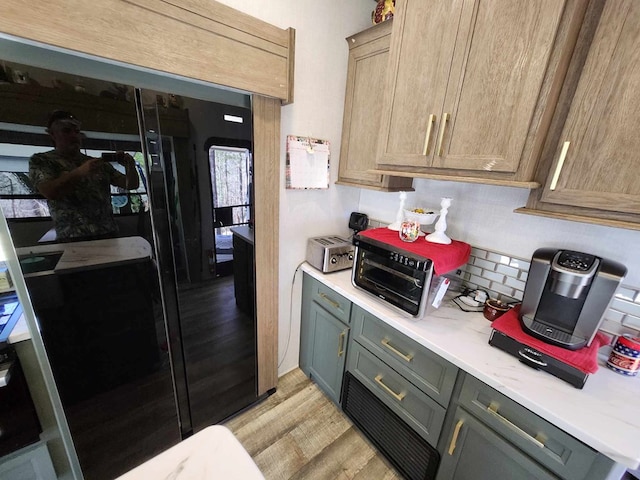 kitchen with light wood-type flooring, light countertops, decorative backsplash, and freestanding refrigerator