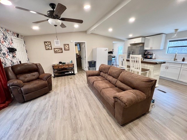 living room with ceiling fan, light hardwood / wood-style floors, sink, and lofted ceiling with beams