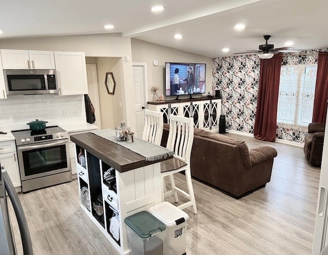 kitchen with appliances with stainless steel finishes, lofted ceiling, decorative backsplash, white cabinets, and light wood-type flooring