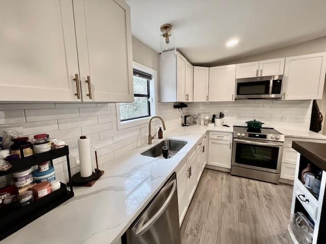 kitchen with decorative backsplash, stainless steel appliances, sink, pendant lighting, and white cabinets