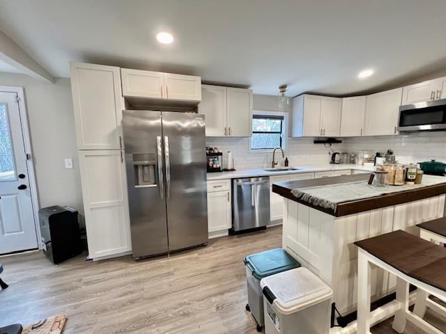 kitchen with white cabinets, light hardwood / wood-style flooring, stainless steel appliances, and tasteful backsplash