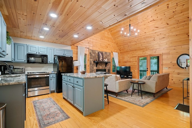 kitchen with black appliances, wooden walls, light wood-type flooring, a kitchen island, and a breakfast bar area