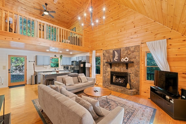 living room with wooden ceiling, high vaulted ceiling, a stone fireplace, wooden walls, and light hardwood / wood-style flooring