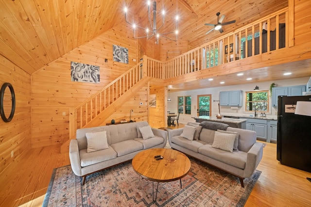 living room with light wood-type flooring, wooden walls, sink, high vaulted ceiling, and wooden ceiling