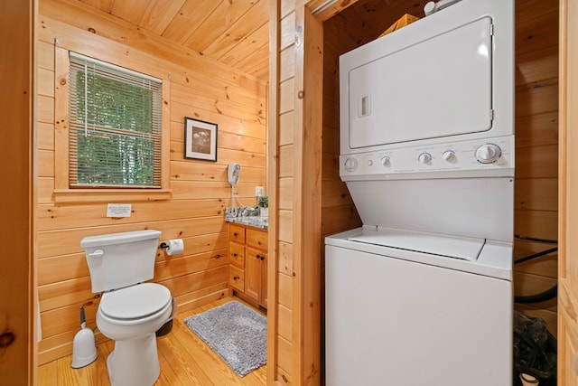 washroom with wood walls, light wood-type flooring, stacked washer / dryer, and wood ceiling