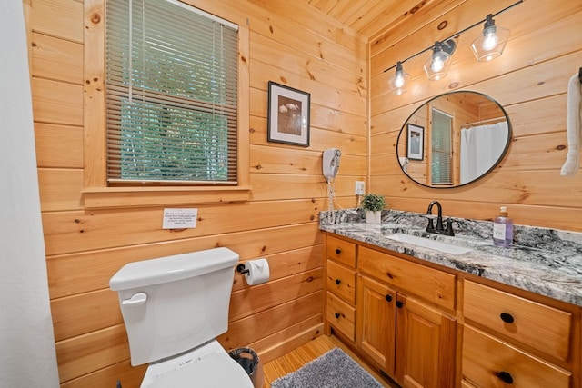 bathroom featuring walk in shower, wooden walls, vanity, and toilet